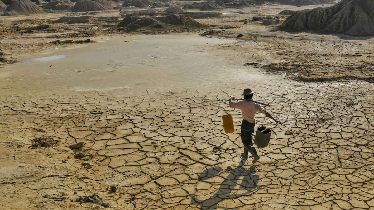 Dryland drought landscape with cracked soil and a person carrying water containers across a dry, barren desert